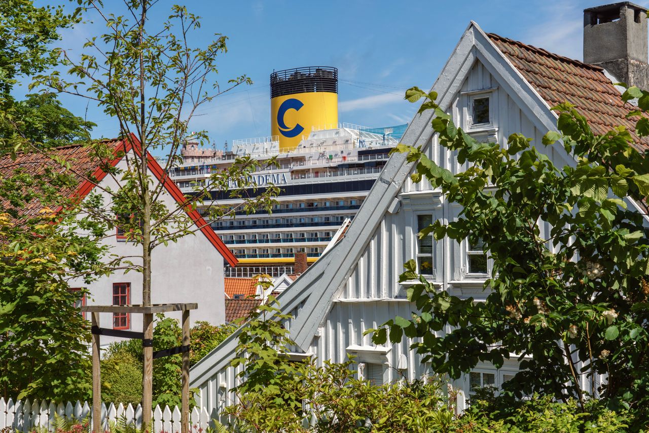 White wooden houses and leafy gardens in Stavanger, with a cruise ship in the background